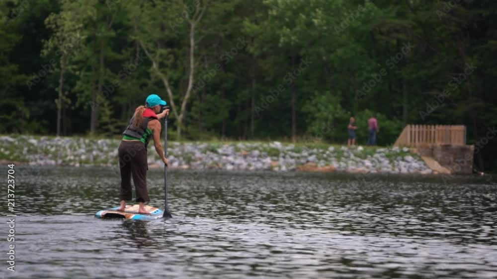 Mature woman on a paddle board going away from the camera on a mountain lake. Mature woman on a paddle board going away from the camera on a mountain lake.