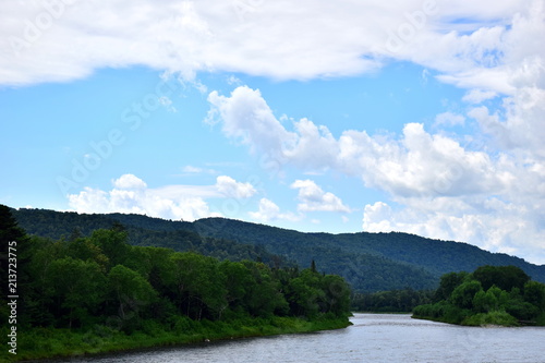 River in the middle of the green mountains Sikhote-Alin. Green hills, lots of forest, blue sky and white clouds. River leaving into the distance of the hills. © Liudmila