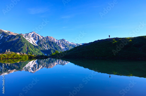 朝日を浴びた新緑の八方池と登山者