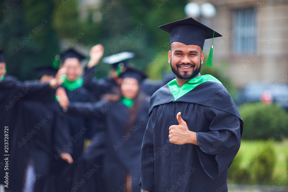 portrait of successful indian student in graduation gown thumb up Stock