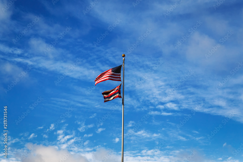 Hawaiian and American flags on a blue cloudy sky background