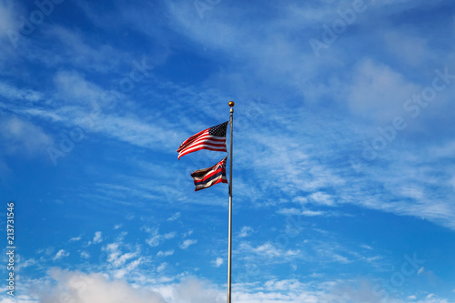 Hawaiian and American flags on a blue cloudy sky background