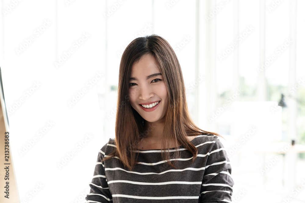 Portrait of young attractive asian creative woman or designer smiling and looking at camera in modern office feeling confident in casual outfit. Headshot of female employee, entrepreneur or student. Portrait of young attractive asian creative woman or designer smiling and looking at camera in modern office feeling confident in casual outfit. Headshot of female employee, entrepreneur or student.