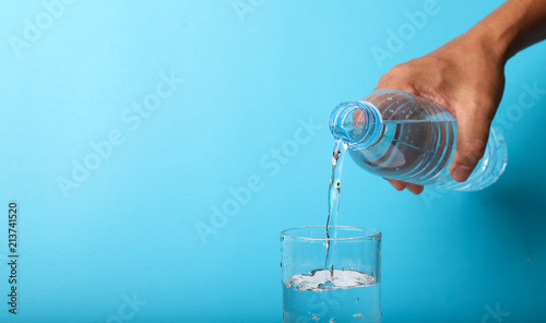 Closeup of pouring mineral water from bottle into glass by hand.