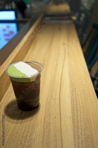 A plastic glass of iced tea with layer of cream cheese foam, Trendy food and drinks, Cheese Tea with three whipped cream cheese consists of matcha, chocolate and vanilla. on wooden table