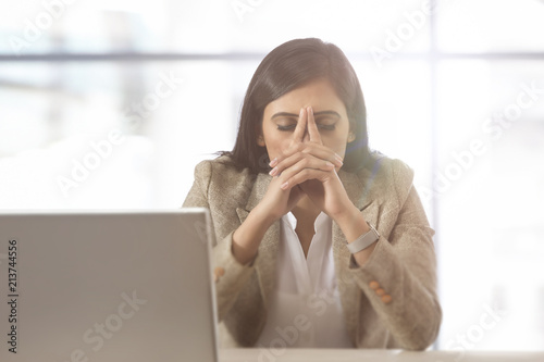 Stressed businesswoman at laptop with head in hands
