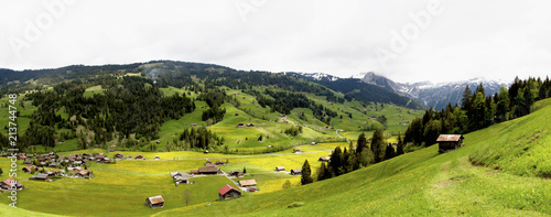 Gstaad Wintermatte Chalet Village – Spectacular Super wide panorama – Beautiful Swiss chalet village & scattered chalets– super-pollination has resulted in humungous numbers of yellow wildflowers.