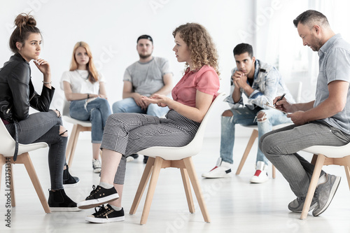 Young woman resolving problem with rebellious friend during group therapy with counselor