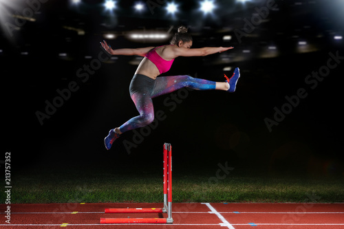 Determined young woman athlete jumping over a hurdles