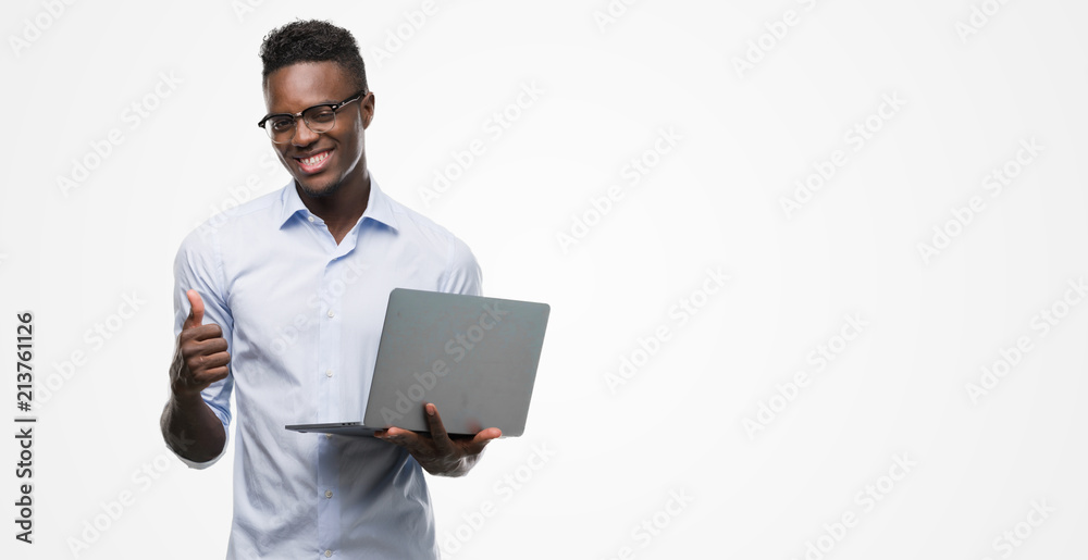 Young african american businessman using computer laptop happy with big smile doing ok sign, thumb up with fingers, excellent sign Young african american businessman using computer laptop happy with big smile doing ok sign, thumb up with fingers, excellent sign