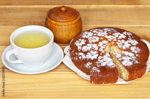Homemade cake decorated with powdered sugar and a cup of green tea on a wooden table