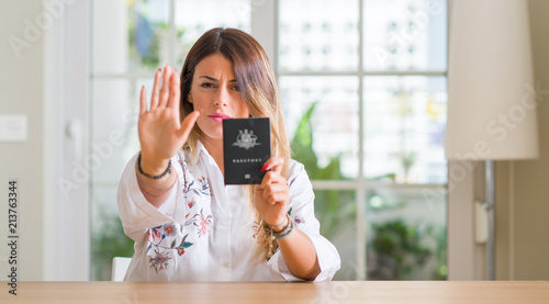 Young woman at home holding a passport of Australia with open hand doing stop sign with serious and confident expression, defense gesture