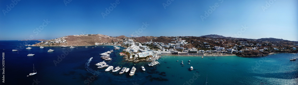 Fototapeta premium Aerial ultra wide panoramic drone view of iconic turquoise clear water beach of Psarou and Platy Yalos with yachts docked, Mykonos island, Cyclades, Aegean, Greece