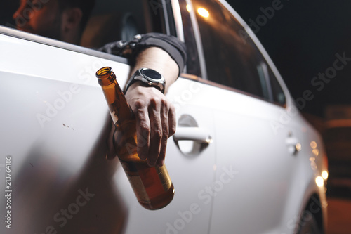 Drunk young man drives a car with a bottle of beer. This is a campaign picture of Don't Drink for Drive. 