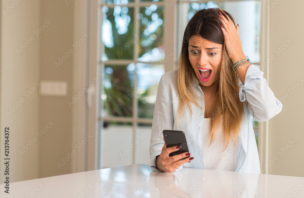 Young woman holding smartphone surprised. Panic and shock emotion at home