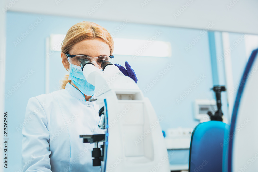Professional research. Serious lab assistant bowing head while working with microscope Professional research. Serious lab assistant bowing head while working with microscope