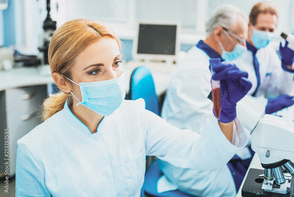 Let me think. Attractive blonde wearing face mask while looking at test tube Let me think. Attractive blonde wearing face mask while looking at test tube