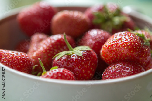 ripe strawberry berry with green leafs in a plate on a green background