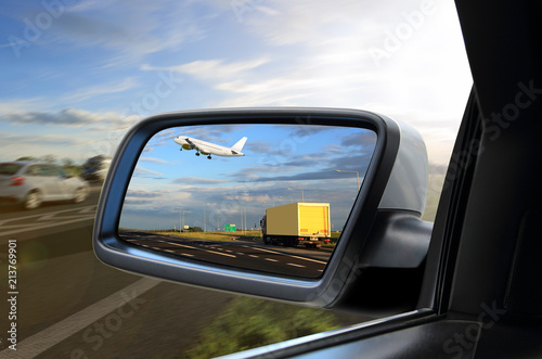 Widok w lusterku samochodu osobowego jak samolot wznosi sią nad ciężarówką .