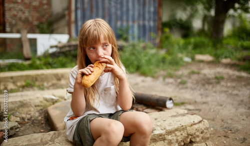 Photos Poor homeless girl eating a piece of bread in the dirty alley