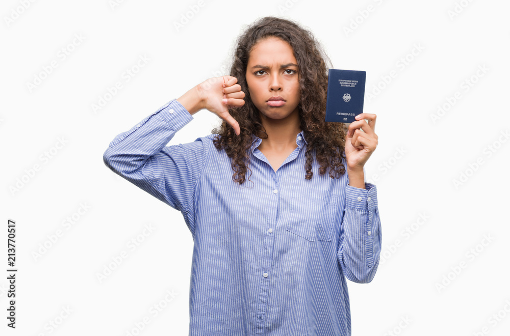 Young hispanic woman holding passport of Germany with angry face, negative sign showing dislike with thumbs down, rejection concept Young hispanic woman holding passport of Germany with angry face, negative sign showing dislike with thumbs down, rejection concept