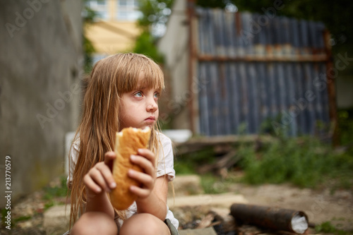 Photography Portrait of hungry homeless girl eating a piece of bread in the dirty alley