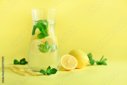 Fresh summer fruits water or lemonade with mint, ice, lemon on yellow background. Copy space. Summer infused water. Citrus flavored beverage.