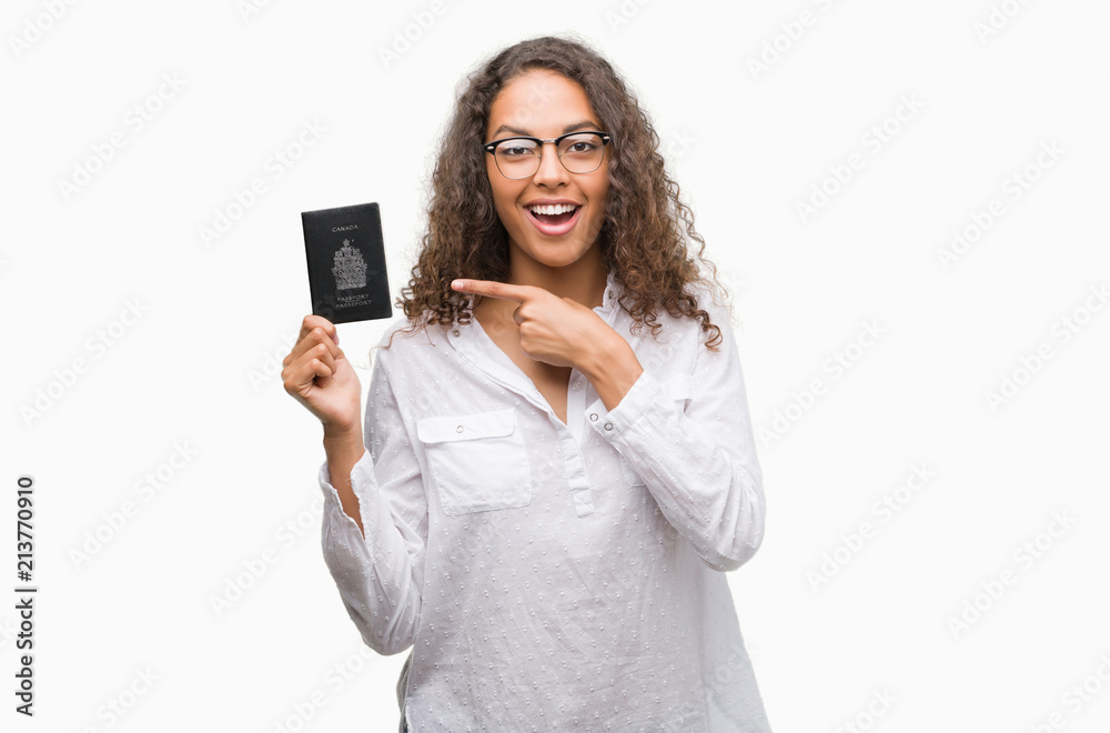 Young hispanic woman holding passport of Canada very happy pointing with hand and finger Young hispanic woman holding passport of Canada very happy pointing with hand and finger