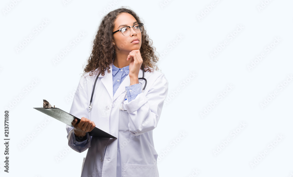 Young hispanic doctor woman holding a clipboard serious face thinking about question, very confused idea