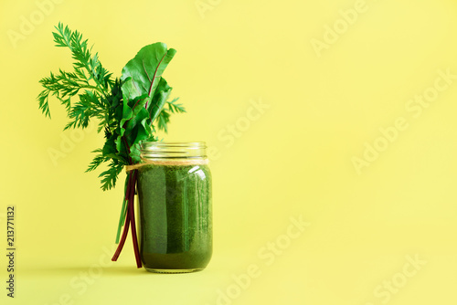 Smoothie with beet greens and carrot tops on yellow background, copy space. Summer vegan food concept. Healthy detox eating, alkaline diet. Fresh squeezed juice, drink from vegetables. Leafy greens. photo