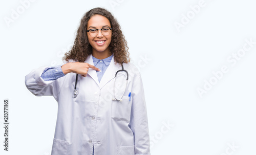Young hispanic doctor woman with surprise face pointing finger to himself