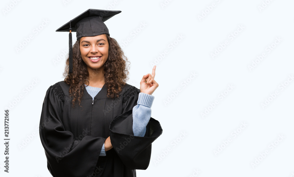 Young hispanic woman wearing graduation uniform very happy pointing with hand and finger to the side Young hispanic woman wearing graduation uniform very happy pointing with hand and finger to the side