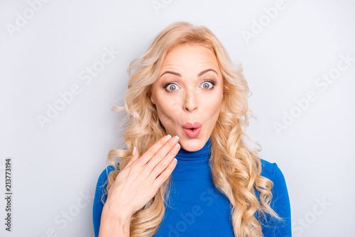 Oops! Portrait of sexy, foxy,  stylish, pretty, cute, charming, nice, blonde woman in blue roll neck  holding palm near pout lips looking at camera isolated on grey background © deagreez