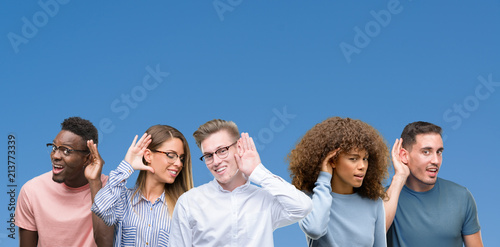 Composition of group of friends over blue blackground smiling with hand over ear listening an hearing to rumor or gossip. Deafness concept. photo