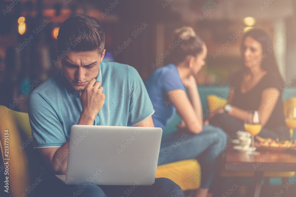 Attractive male is using a laptop and making notes while working in cafe Attractive male is using a laptop and making notes while working in cafe