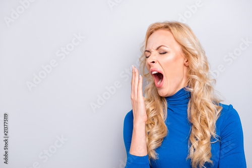 Portrait with copy space, empty place of pretty, trendy, charming, sexy,  tired, cute, woman in blue turtleneck cover her wide open mouth with palm,  having close eyes, very tired want to sleep
