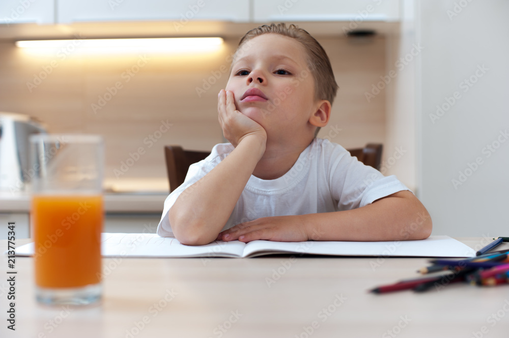 Little thoughtful boy sits at table during coloring with pencils and looks into the camera thinking about something Little thoughtful boy sits at table during coloring with pencils and looks into the camera thinking about something