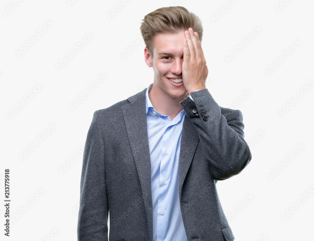 Young handsome blond business man covering one eye with hand with confident smile on face and surprise emotion. Young handsome blond business man covering one eye with hand with confident smile on face and surprise emotion.