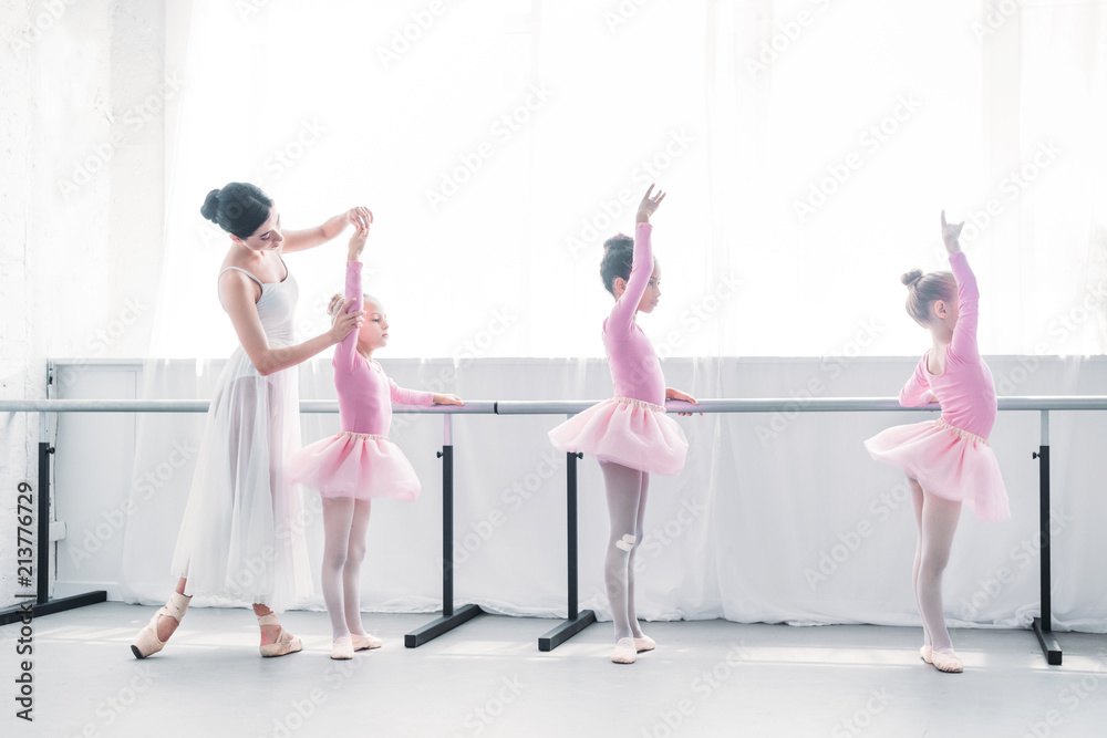 Naklejka premium side view of ballet teacher exercising with children in ballet school
