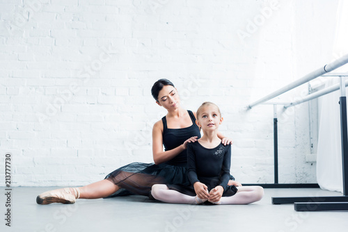 ballet teacher and little student in black clothing exercising together in ballet school