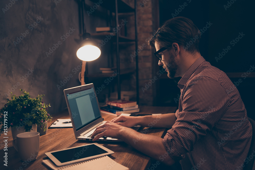 Side view portrait of attractive, hard worker, busy man in shirt with hairstyle, stubble working at night, taking work at home, sitting in workplace, workstation holding hands on keypad Side view portrait of attractive, hard worker, busy man in shirt with hairstyle, stubble working at night, taking work at home, sitting in workplace, workstation holding hands on keypad