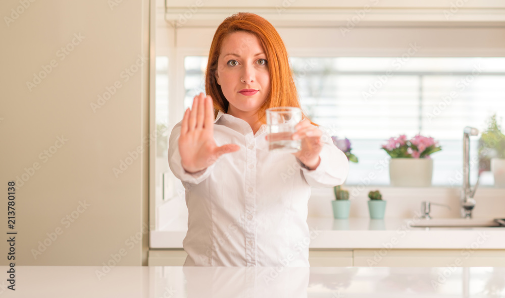 Thirsty redhead woman and glass of water with open hand doing stop sign with serious and confident expression, defense gesture Thirsty redhead woman and glass of water with open hand doing stop sign with serious and confident expression, defense gesture