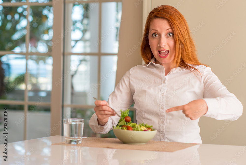 Redhead woman eating fresh green salad at home very happy pointing with hand and finger Redhead woman eating fresh green salad at home very happy pointing with hand and finger