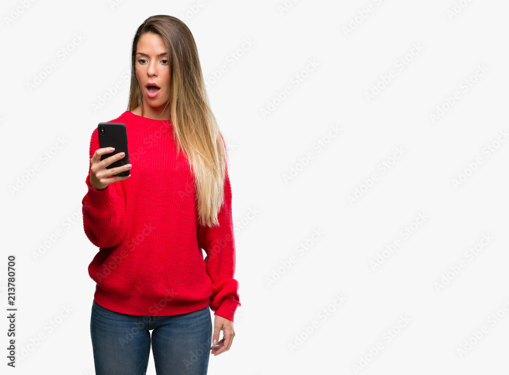 Naklejka premium Beautiful young woman using smartphone scared in shock with a surprise face, afraid and excited with fear expression