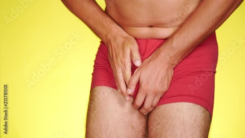 the man has problems with the genitourinary system. guy in red boxers on a yellow background. 4k, close-up, slow-motion shooting.