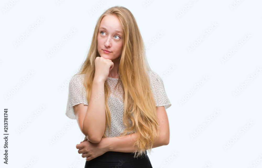 Blonde teenager woman wearing moles shirt with hand on chin thinking about question, pensive expression. Smiling with thoughtful face. Doubt concept. Blonde teenager woman wearing moles shirt with hand on chin thinking about question, pensive expression. Smiling with thoughtful face. Doubt concept.