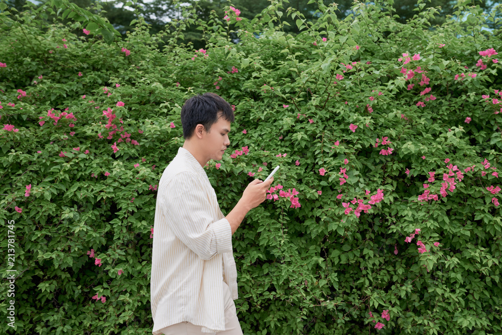 Young asian man in casual clothes on summer day and using smartphone for sending sms