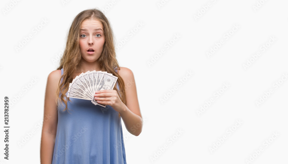 Young blonde woman holding dollars scared in shock with a surprise face, afraid and excited with fear expression Young blonde woman holding dollars scared in shock with a surprise face, afraid and excited with fear expression