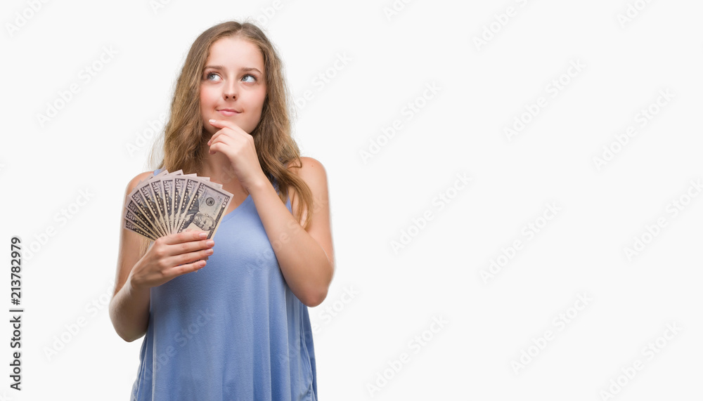 Young blonde woman holding dollars serious face thinking about question, very confused idea Young blonde woman holding dollars serious face thinking about question, very confused idea