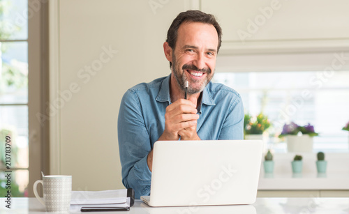 Middle age man using laptop at home with a happy face standing and smiling with a confident smile showing teeth photo